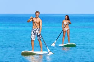 Paddleboard beach people on stand up paddle board surfboard surfing in ocean sea on Big Island, Hawaii Beautiful young multi-ethnic couple, mixed race Asian woman and Caucasian man doing water sport.